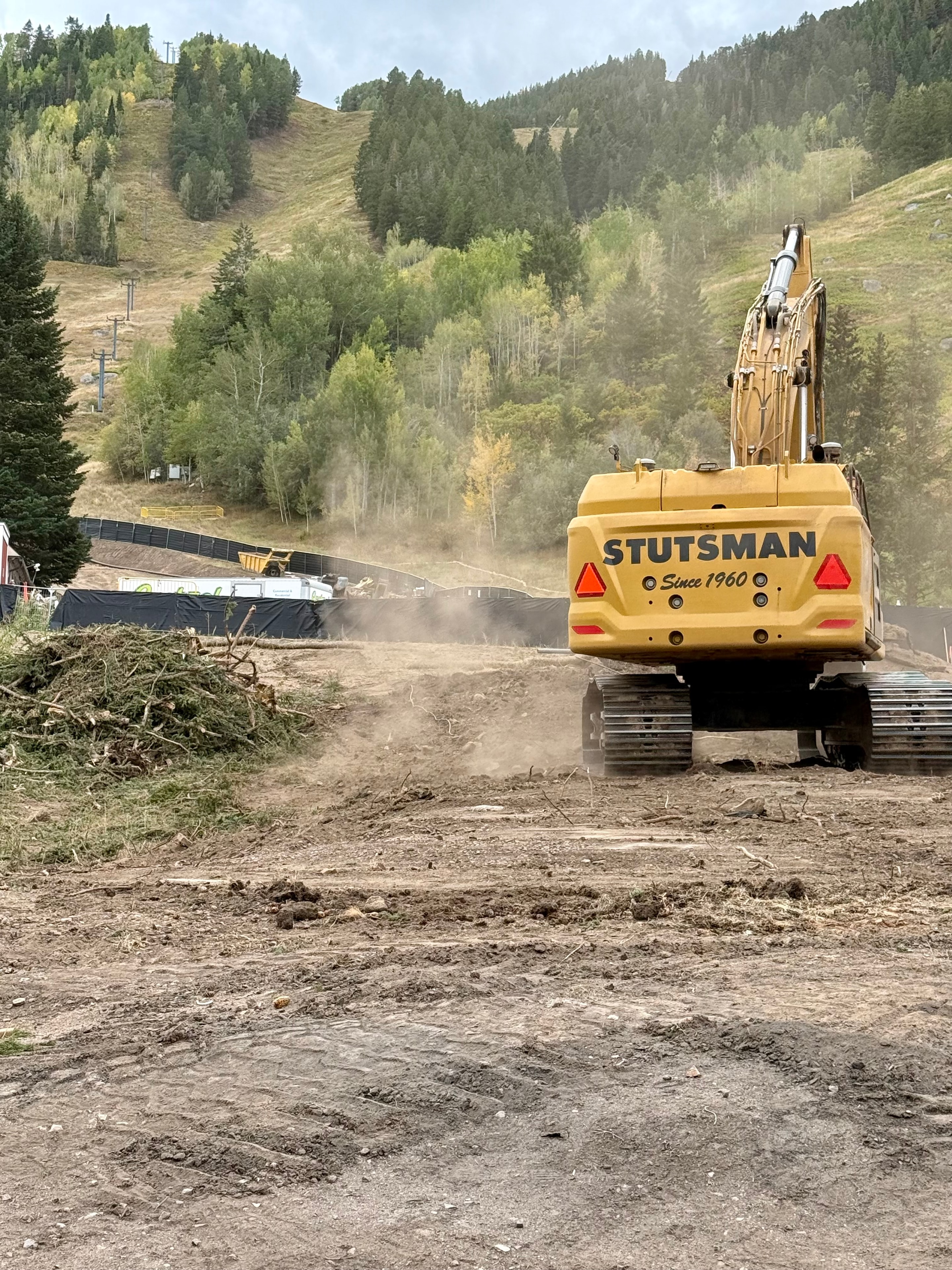 CAT Stutsman excavator at the Lift One and Chalet Alpina construction site with Aspen Mountain hillside in the background, September 8, 2026
